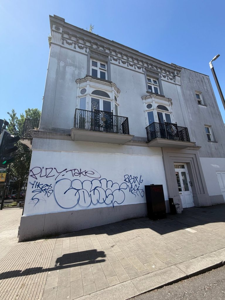 The north wall of The Queen's Head on a sunny day, with graffiti tags across the white ground floor.